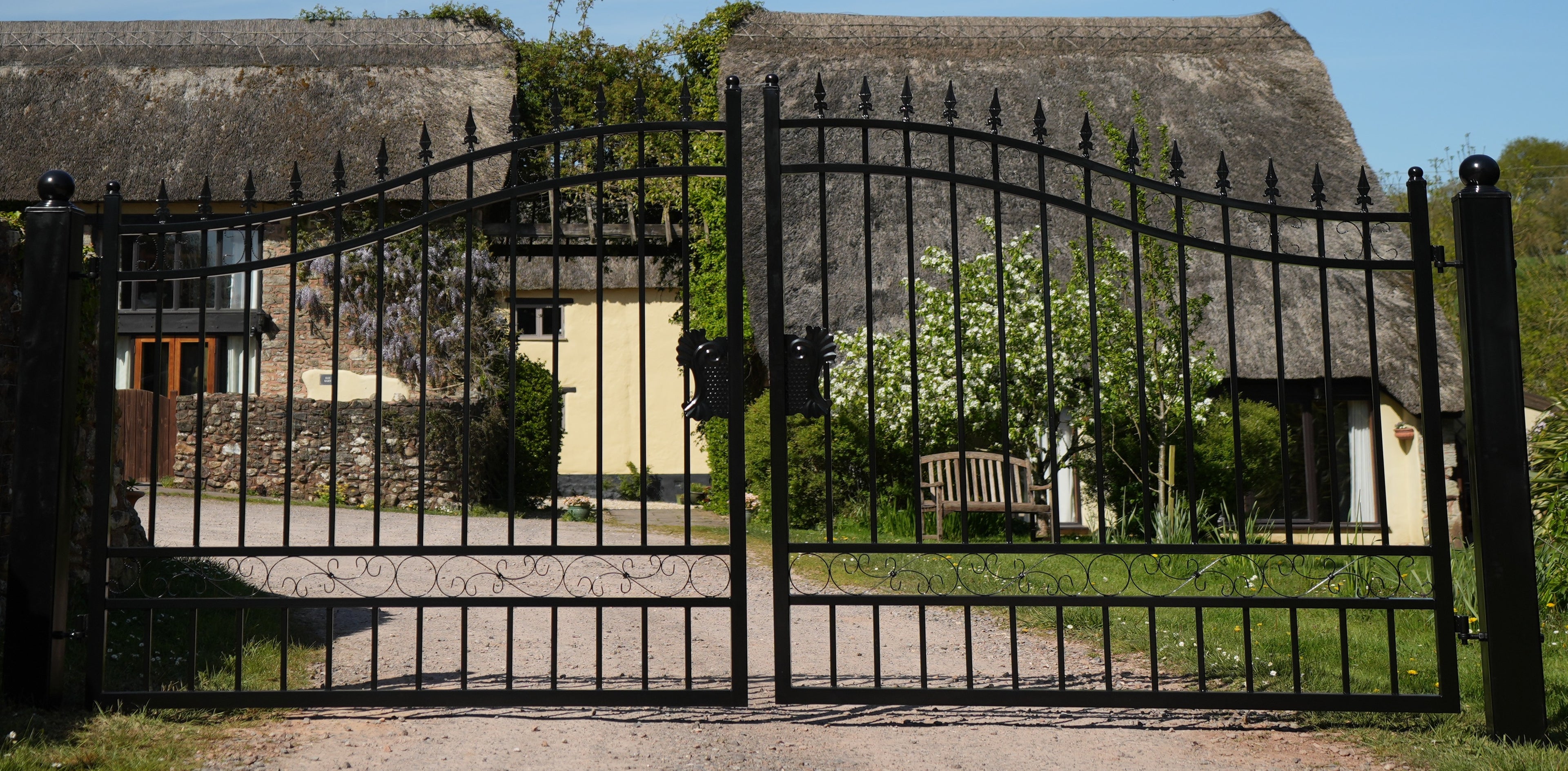 Wrought iron gate leading to a thatched-roof building with greenery around.