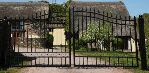 Wrought iron gate leading to a thatched-roof building with greenery around.