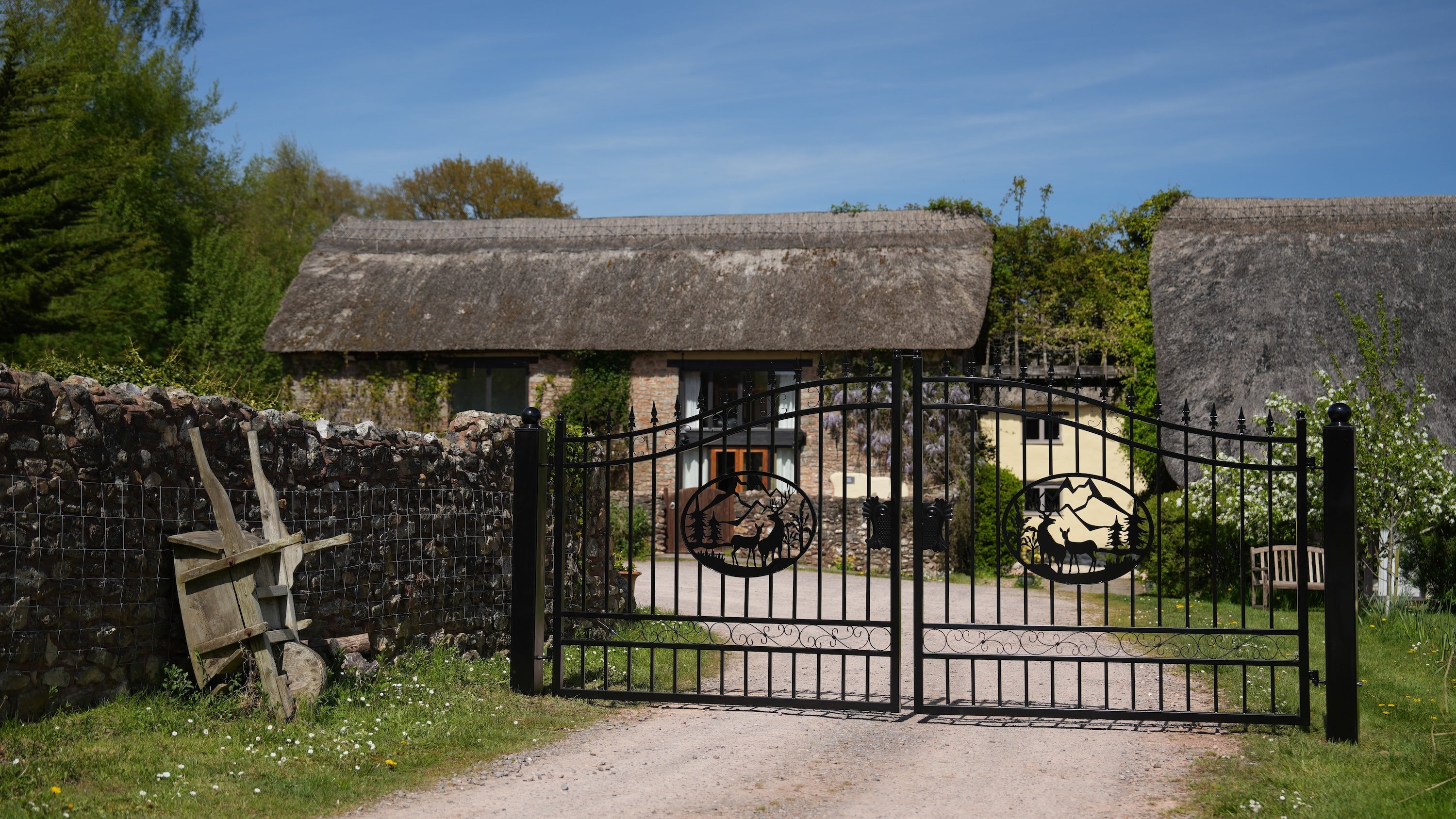 Black metal gate with decorative elements in front of thatched-roof buildings.